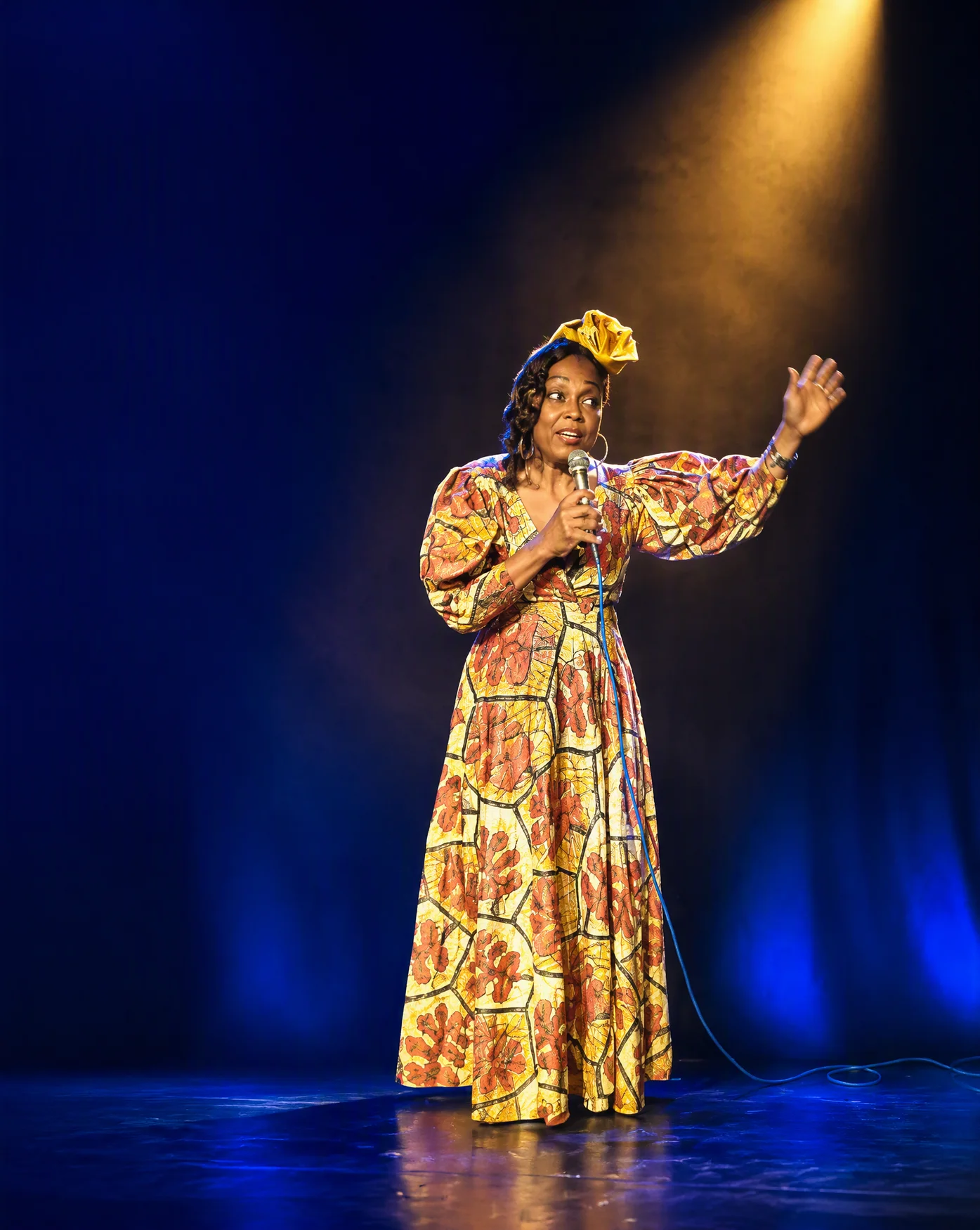 Sharynné Martijn vertelt op een blauw verlicht podium onder een warme gele spotlight